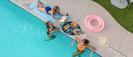 A poolside area with lounge chairs, a pool, and a table with snacks and drinks.