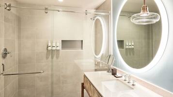 A modern bathroom with a glass-enclosed shower, a vanity with a large mirror, and a round light fixture.
