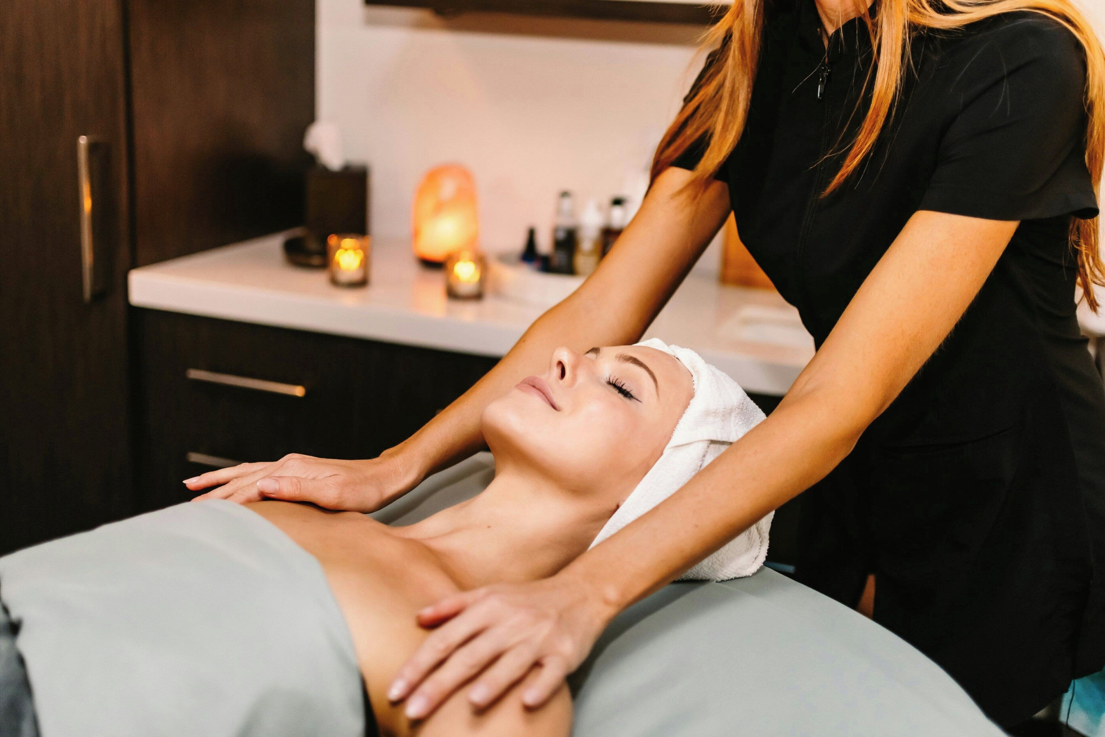 A massage therapy session in a spa setting with a massage table, a towel, and candles in the background.