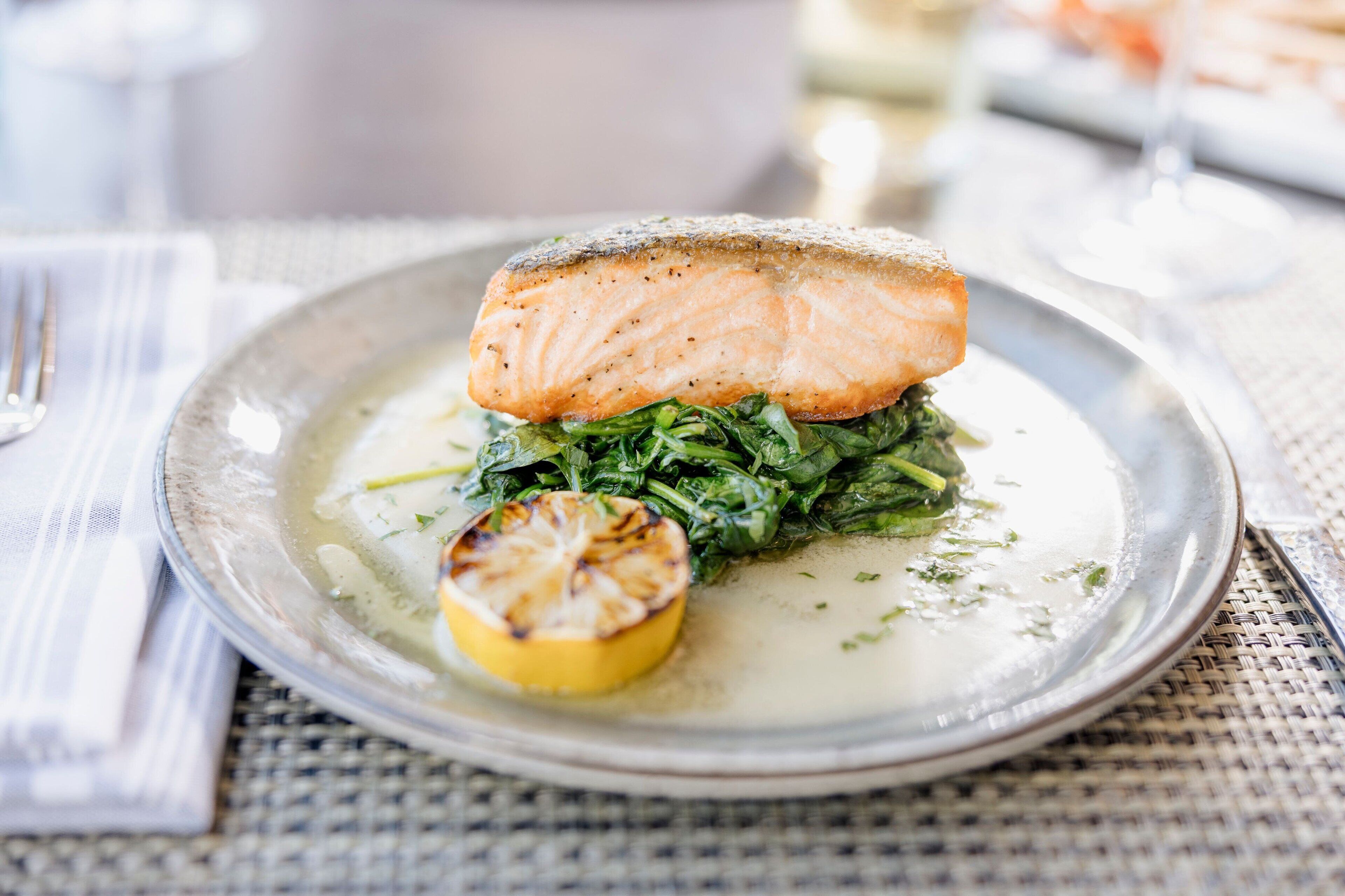 Une assiette contenant un morceau de saumon, des épinards et une demi-tranche de citron grillée.