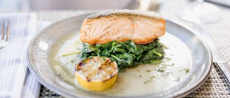 Une assiette contenant un morceau de saumon, des épinards et une demi-tranche de citron grillée.