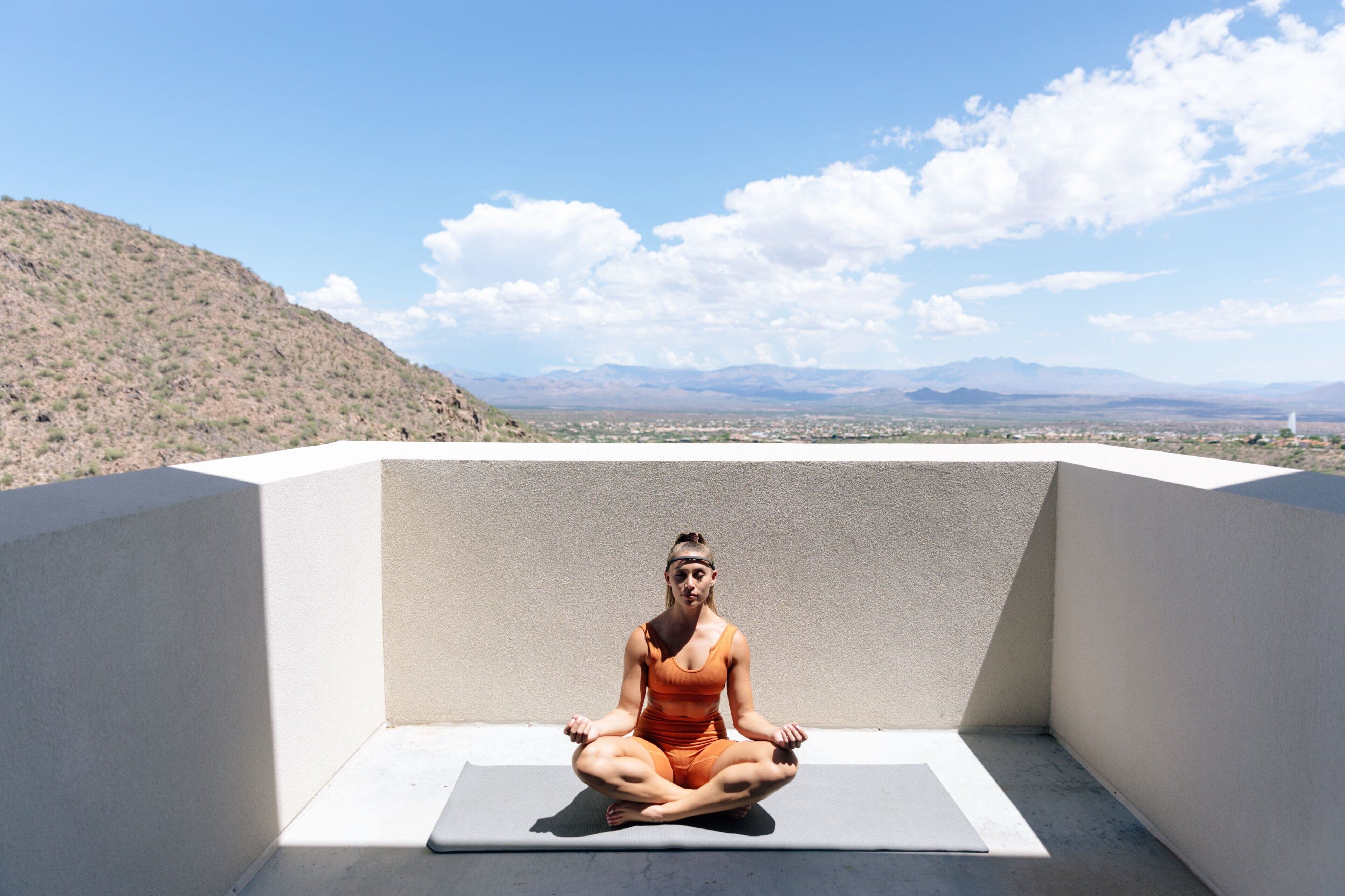 A person meditating on a rooftop with a view of mountains and a clear sky.