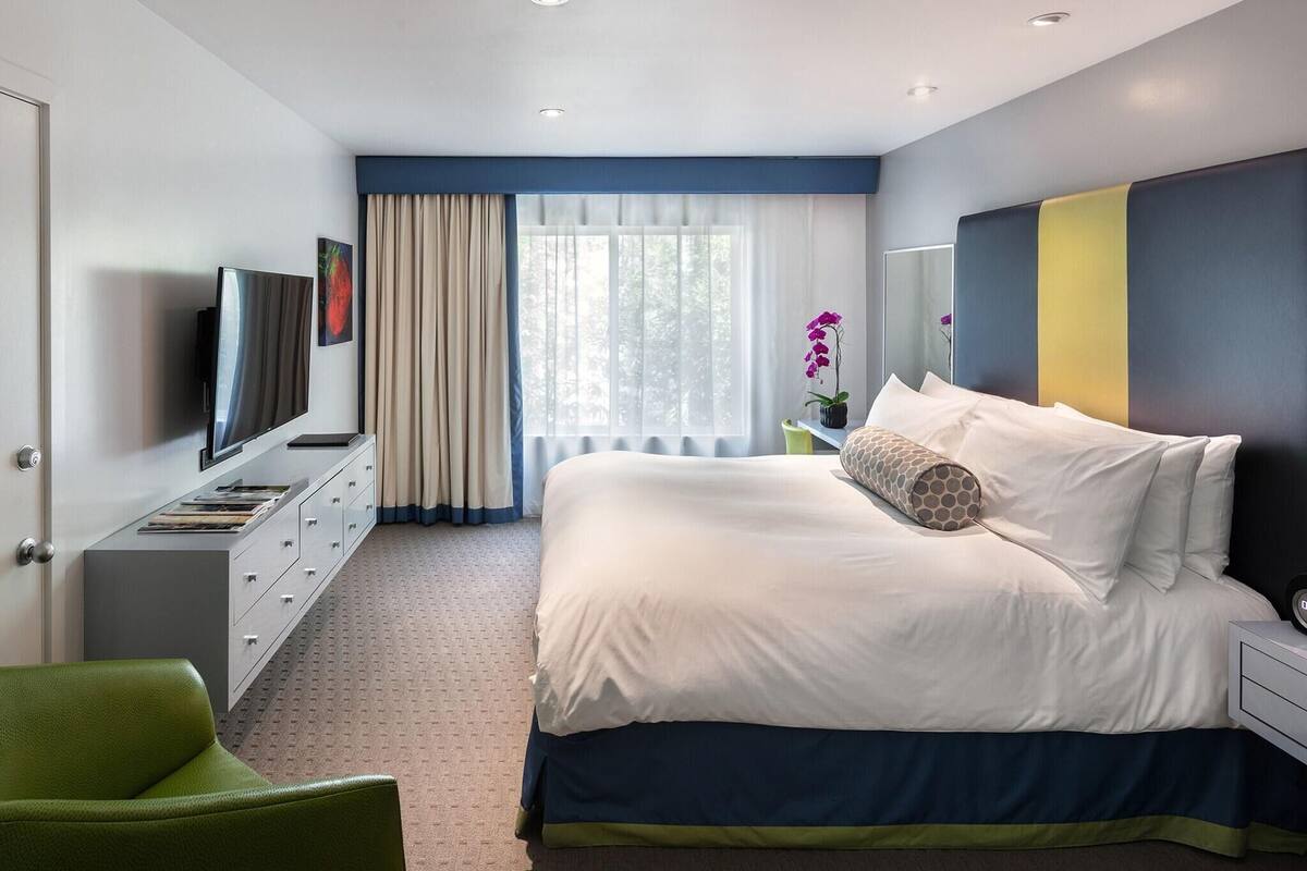 A modern hotel room with a bed, a television, a desk, and a green chair.