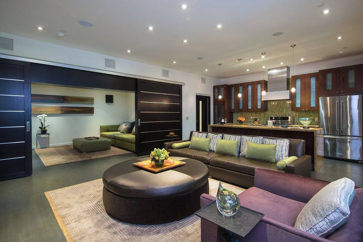 A modern living room with a sofa, ottoman, and coffee table, a kitchen with stainless steel appliances, and a sliding door closet.