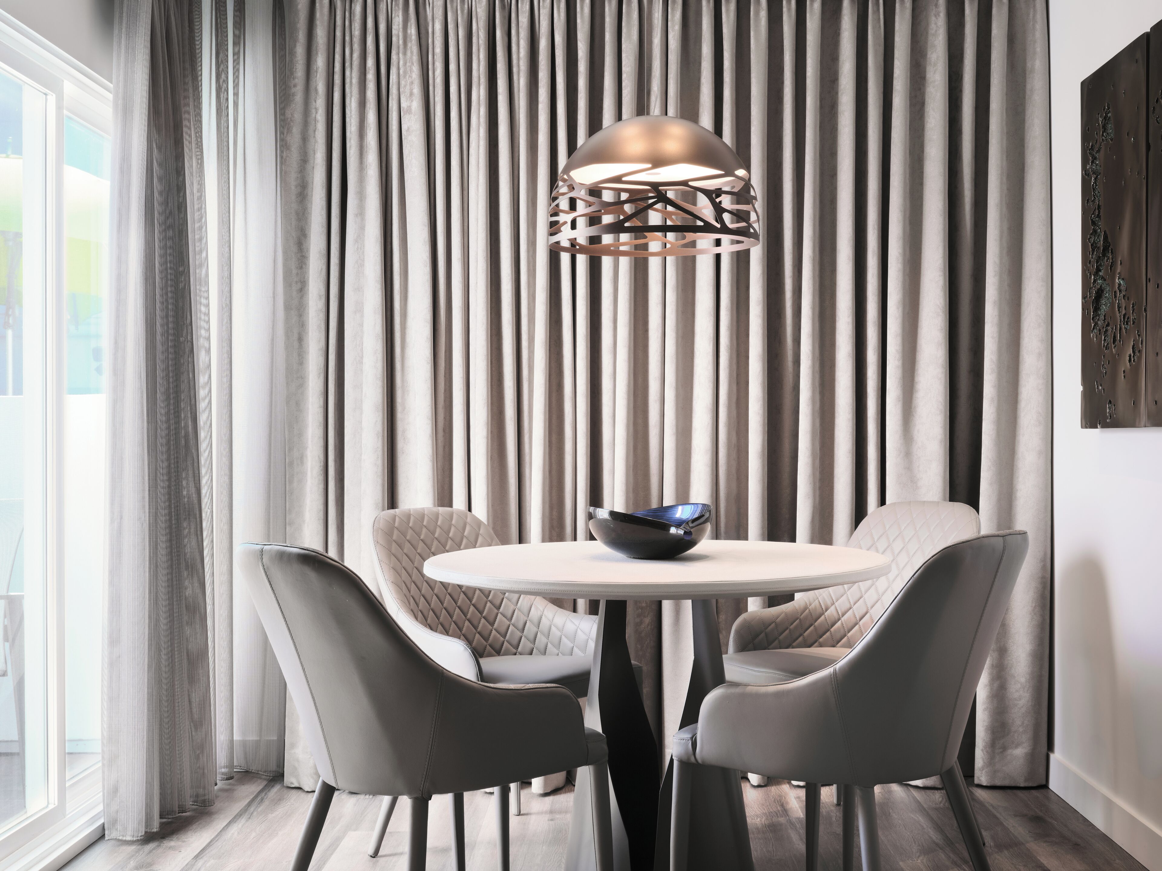 A modern dining area with a round table, four chairs, and a decorative light fixture.