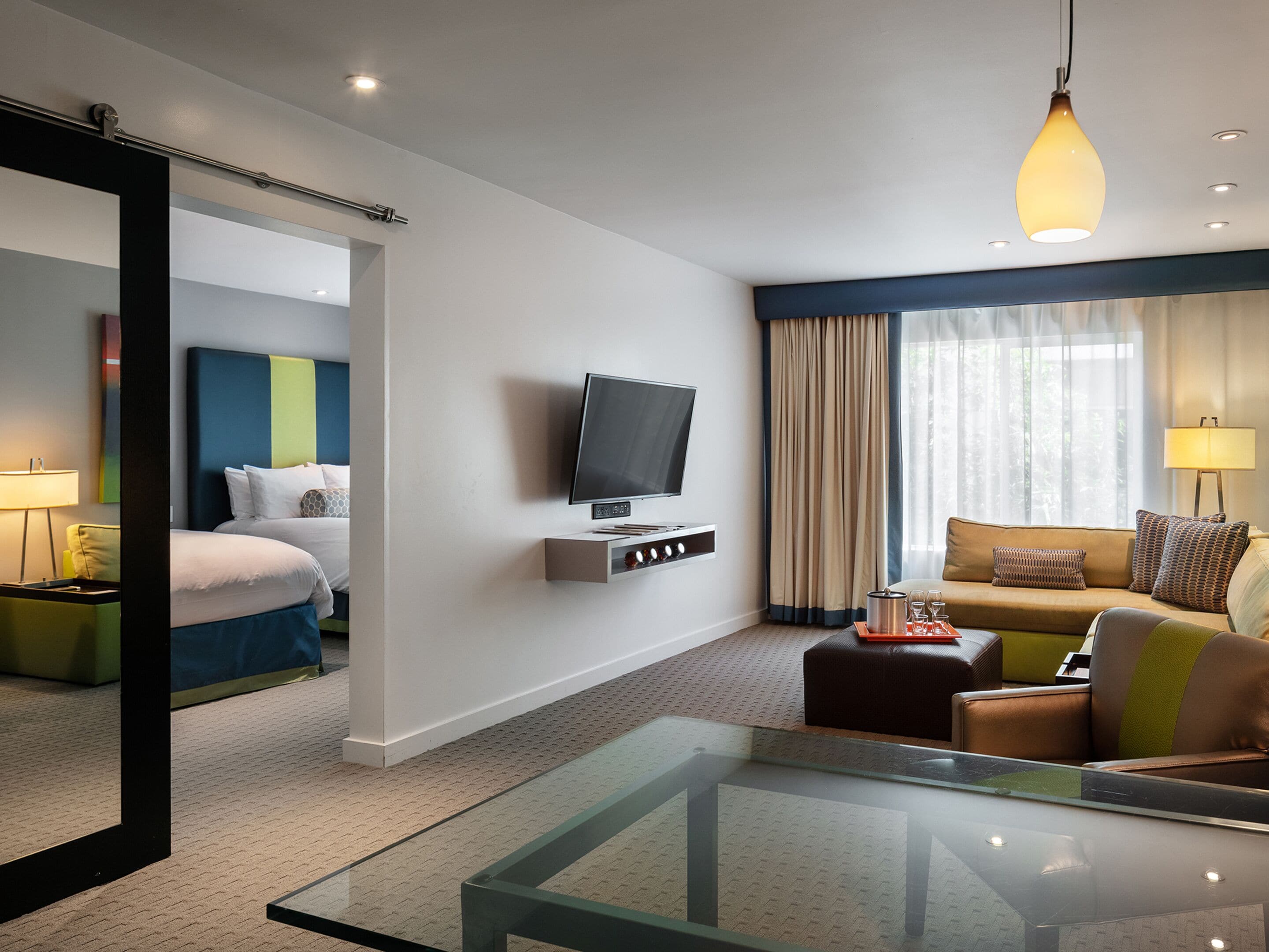 A hotel room with a bed, a television, a sofa, a glass table, and a mirror.