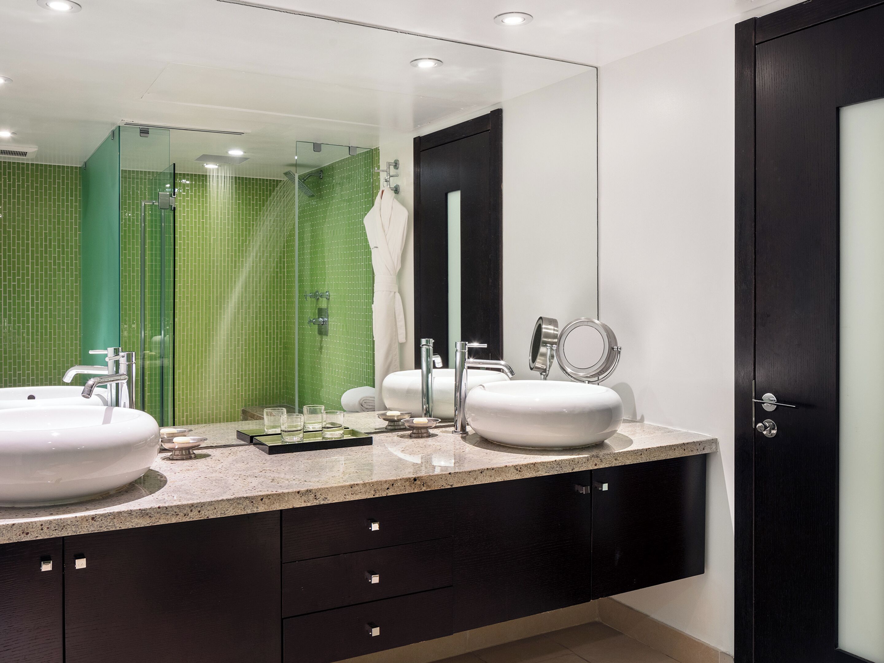 A modern bathroom with two sinks, a glass shower enclosure, and a dark wooden door.