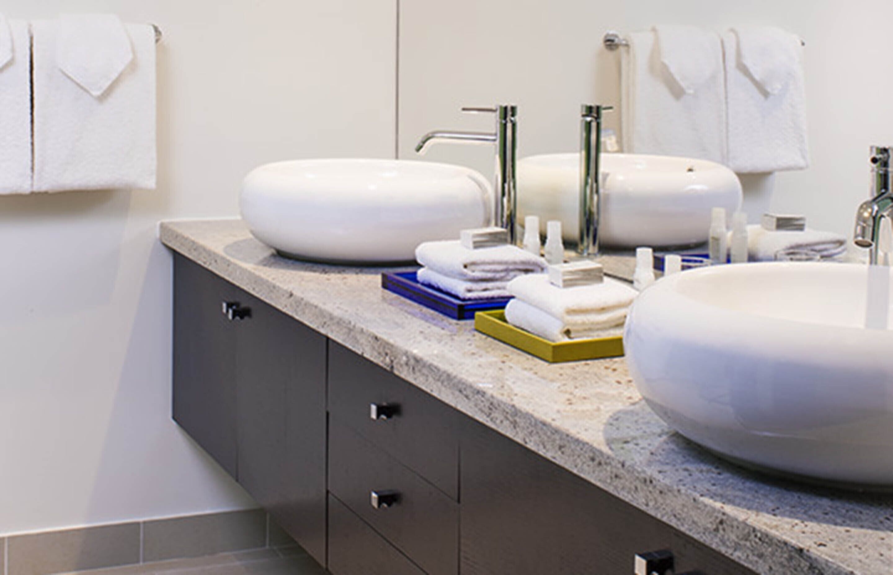 A modern bathroom with two sinks, a mirror, and a countertop with toiletries.