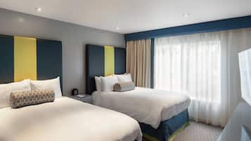 Une chambre d’hôtel avec deux lits, une table de chevet et une grande fenêtre avec des rideaux légers.
