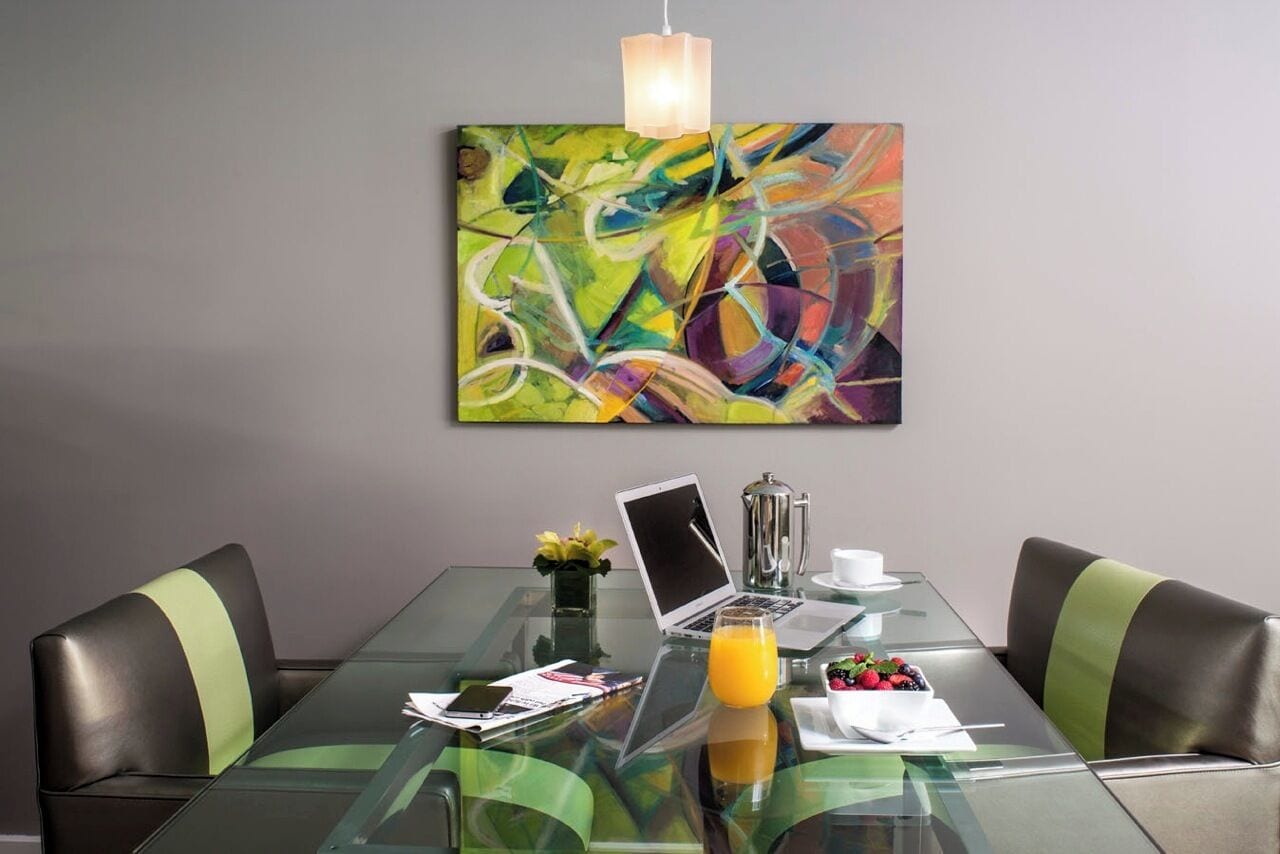 Un coin repas moderne avec une table en verre, deux chaises, un ordinateur portable, une cafetière et un saladier rempli de fruits.