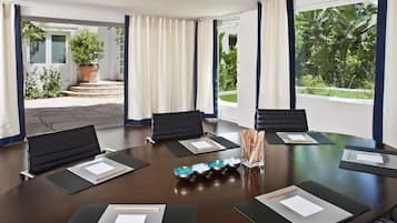 Un salón de conferencias con una gran mesa, sillas negras y vistas a un jardín a través de amplios ventanales.
