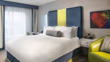 A hotel room with a large bed, a bedside table with a radio, a green armchair, and a painting of a heart on the wall.