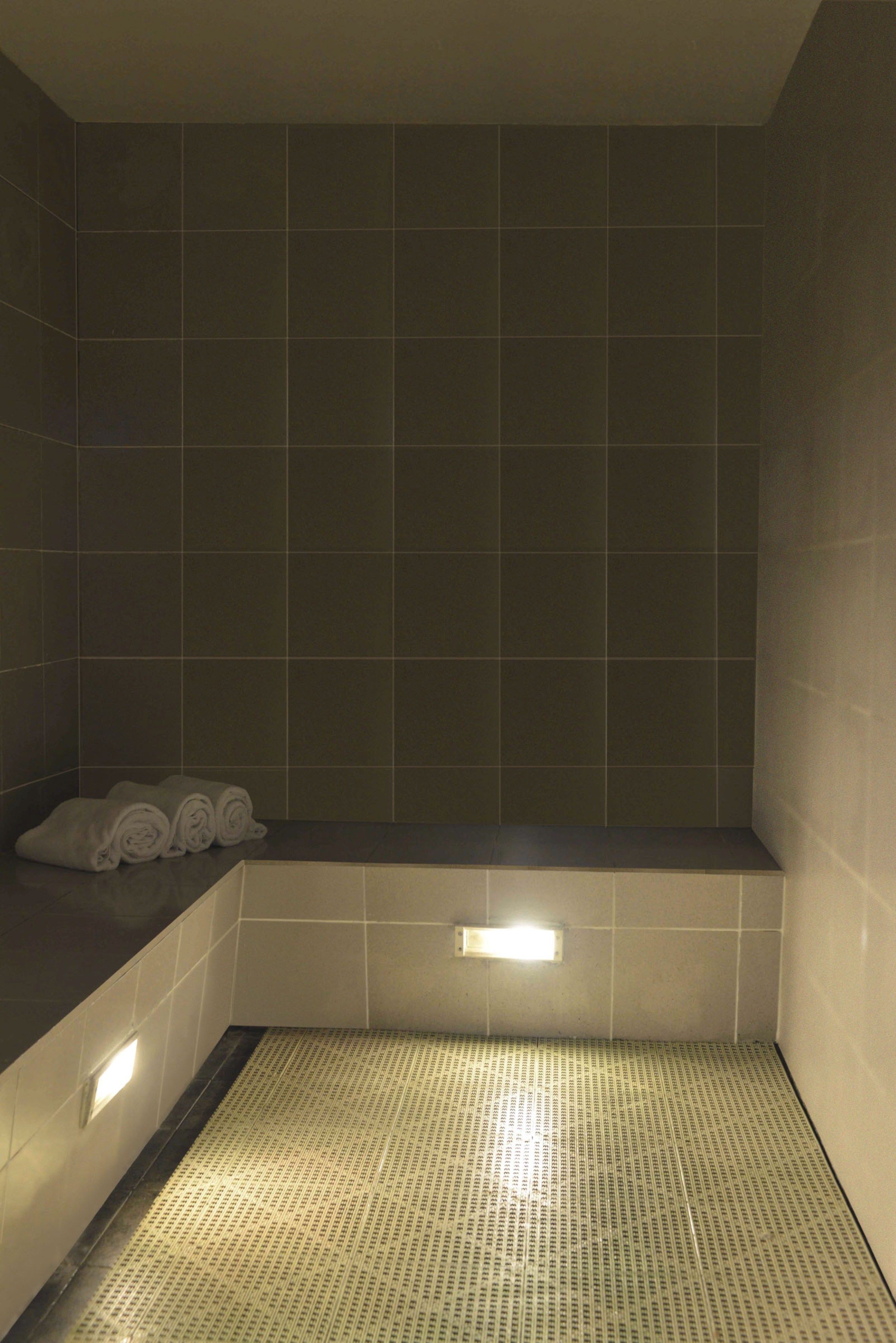 A small, dimly lit bathroom with dark tiles, a bench, and a tiled floor.