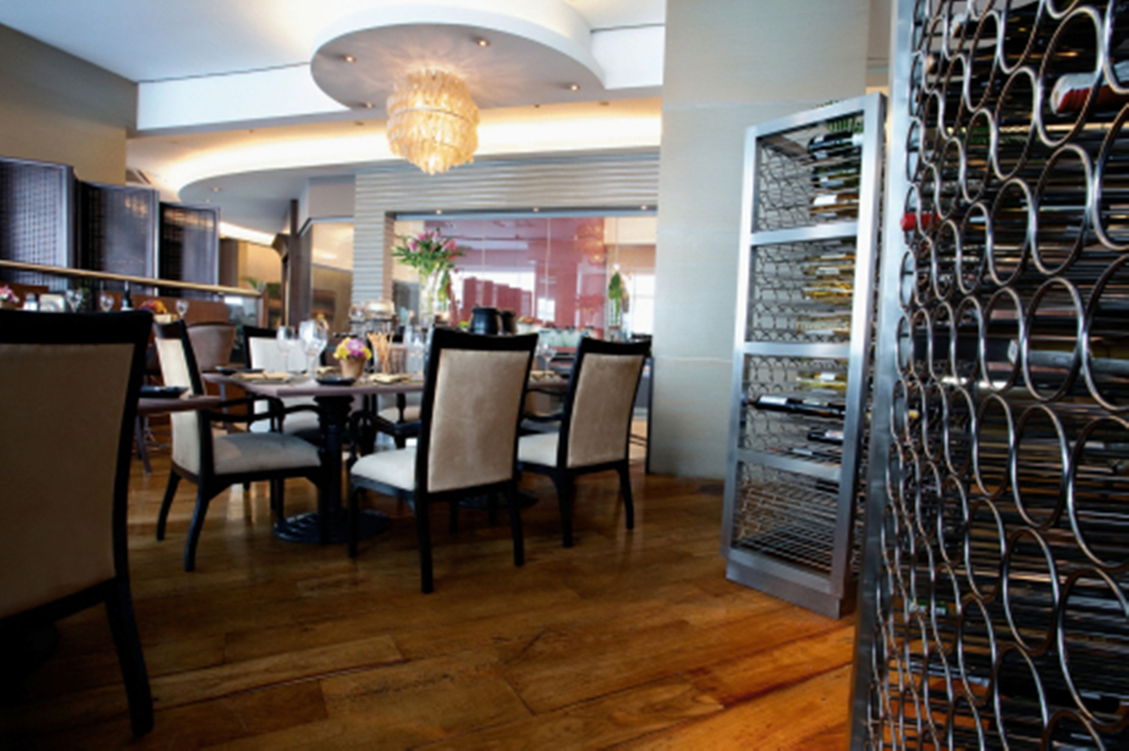 A dining area with a chandelier, wooden flooring, and a metal rack with items.