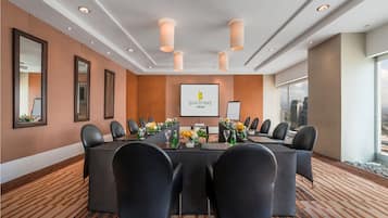 Un salón de conferencias con una larga mesa, sillas negras y una pantalla que muestra el logotipo.