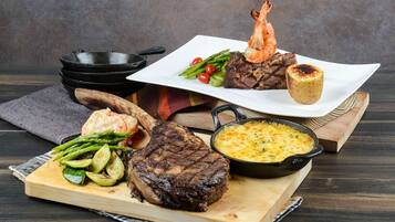 A variety of dishes including steak, shrimp, asparagus, and a baked potato on a wooden board.