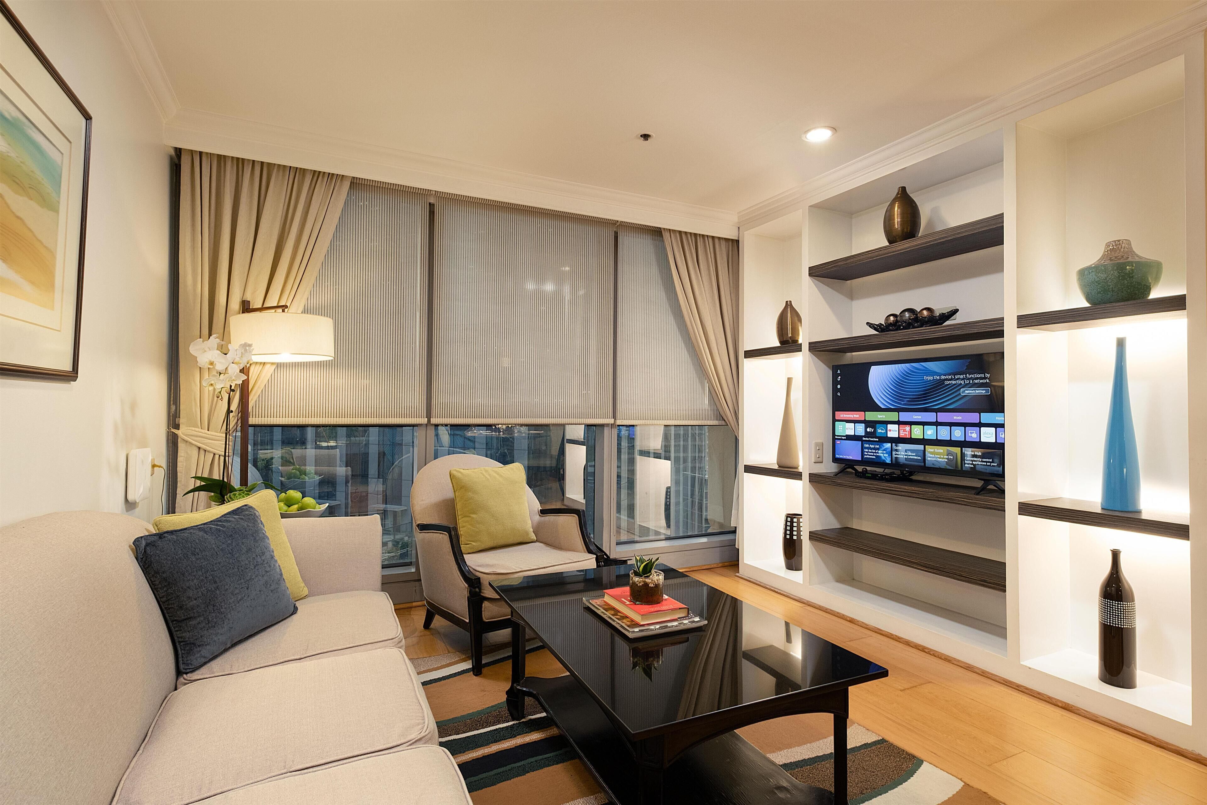 A modern living room with a sofa, armchair, coffee table, and a flat-screen TV mounted on a wall.