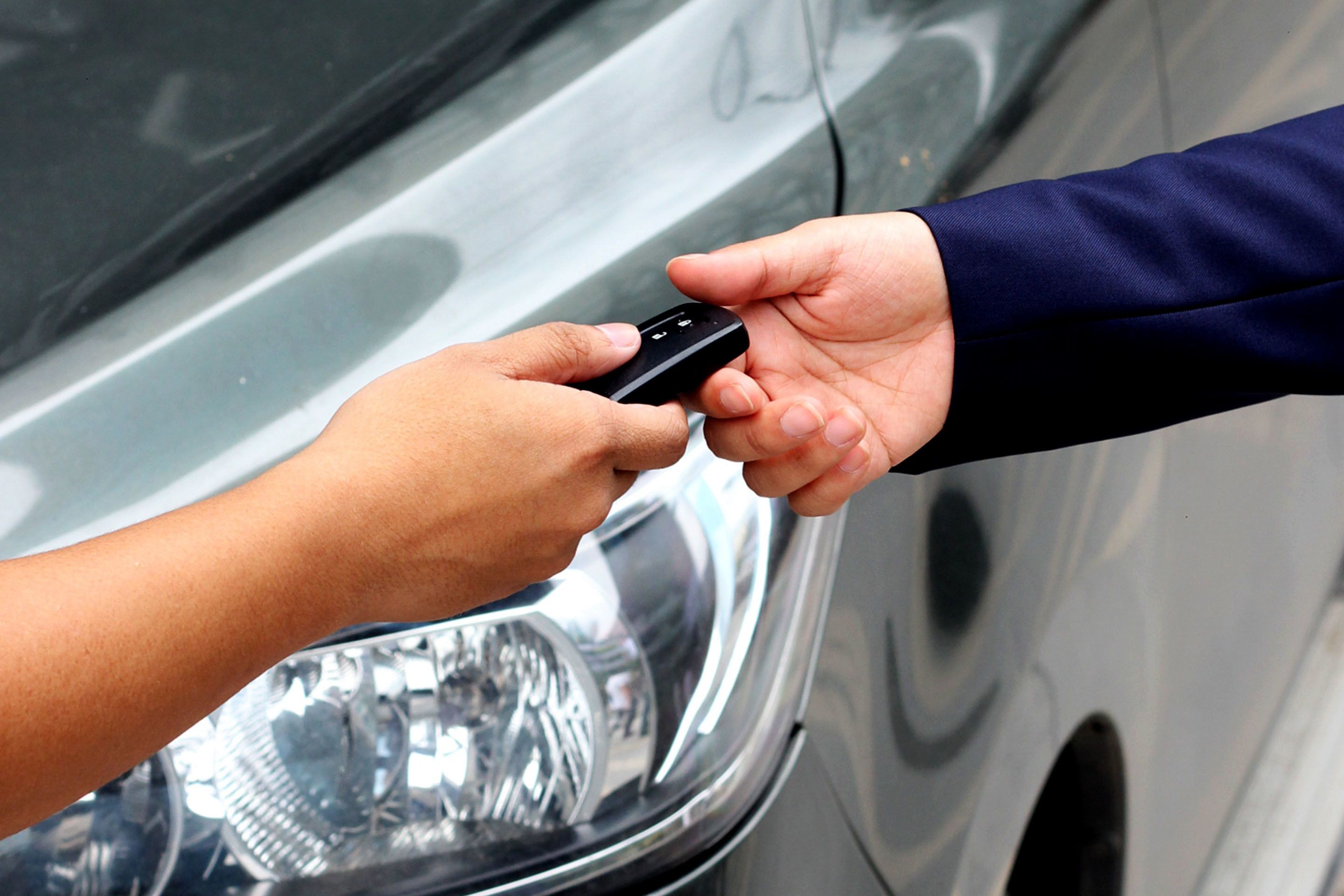 A hand holding a car key fob near a car's door handle.