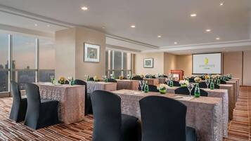 A conference room with tables set for a meeting, a projector screen, and framed pictures on the walls.