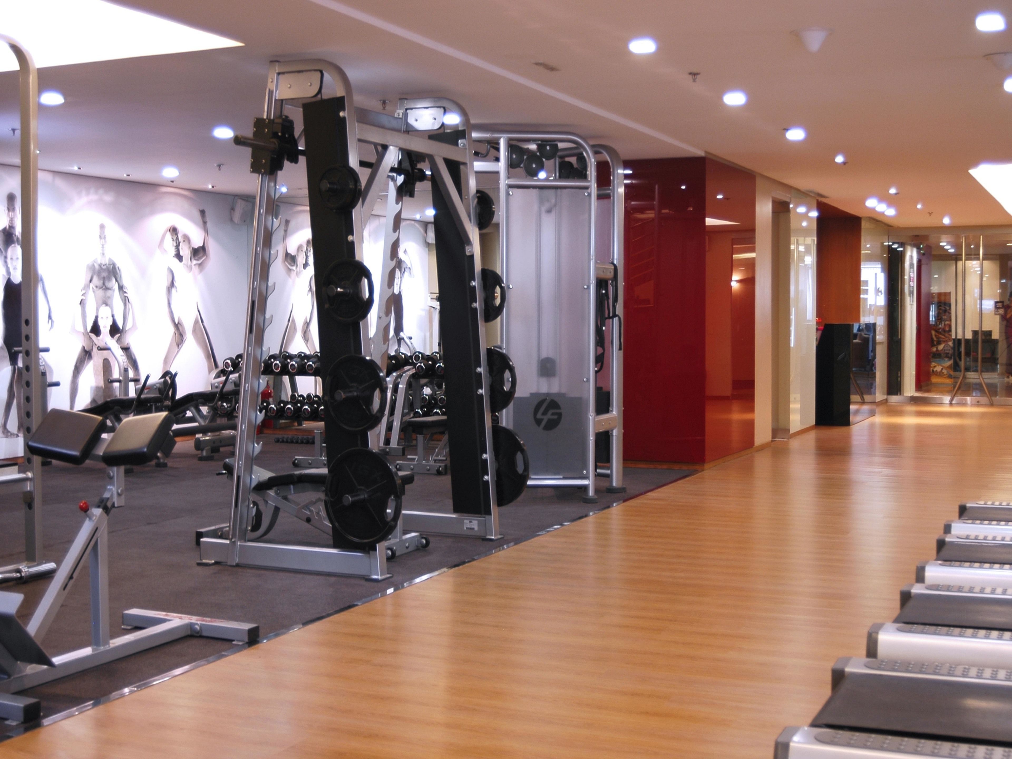 A gym with exercise equipment, treadmills, and a wall with fitness posters.