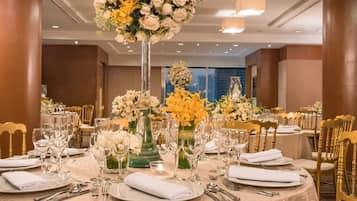 A banquet hall with round tables set for dining, featuring floral centerpieces and gold chairs.