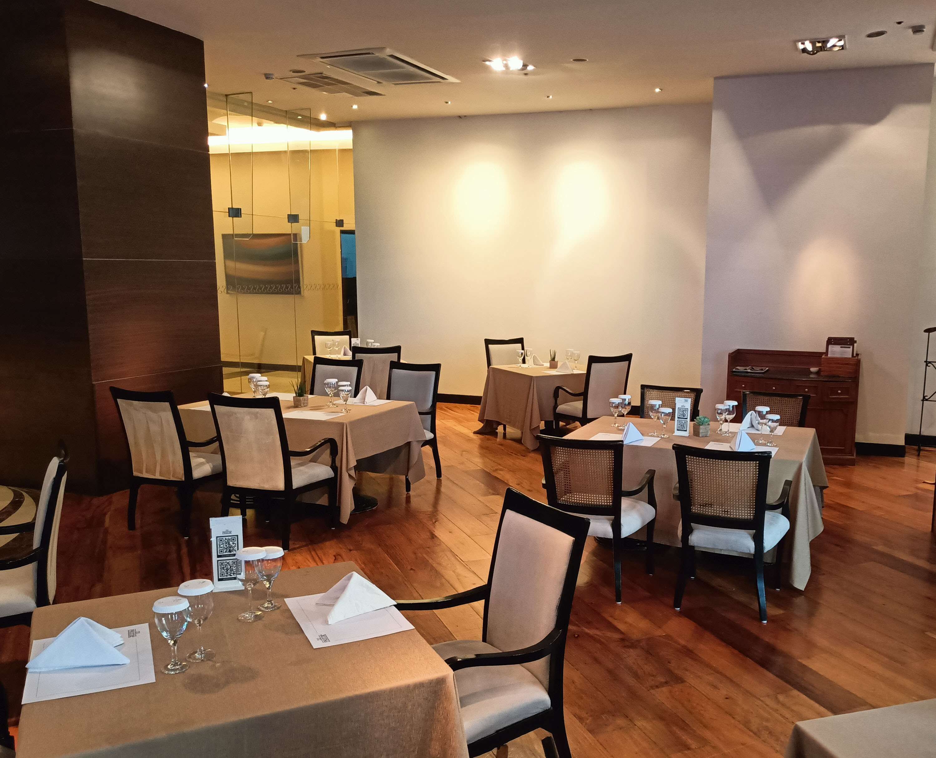 A dining area with multiple tables set for guests, equipped with wine glasses and menus.