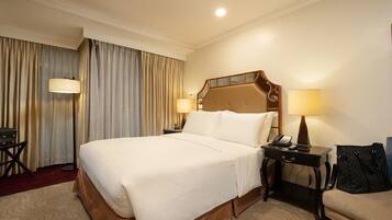 A hotel room with a large bed, two bedside lamps, a desk with a telephone, and a chair.