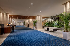 Un hall d’hôtel avec un tapis bleu, des espaces aménagés pour s’asseoir, un comptoir d’accueil et un escalier.