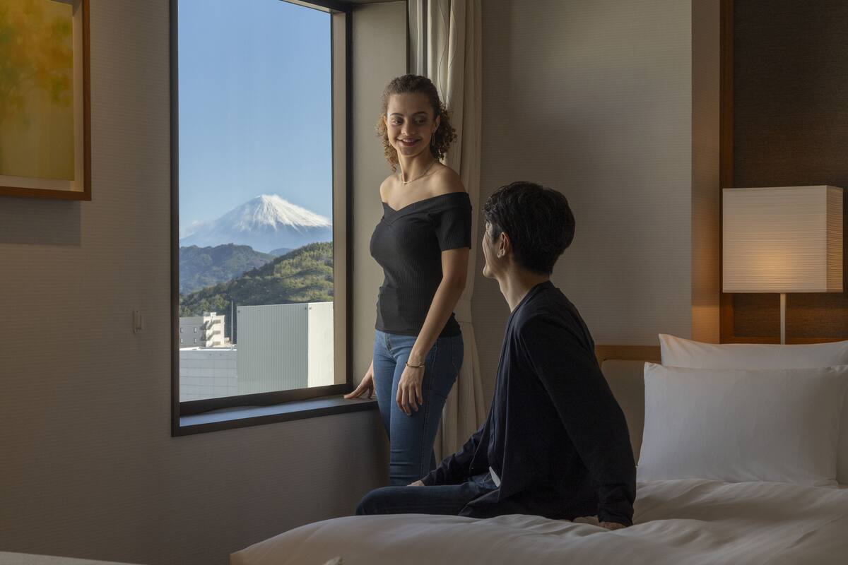 Une chambre d’hôtel avec un lit, une fenêtre donnant sur une montagne et une lampe de chevet.
