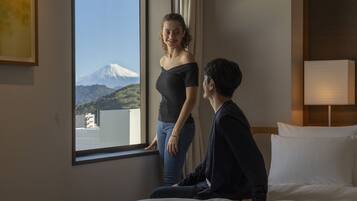 A hotel room with a bed, a window with a view of a mountain, and a bedside lamp.