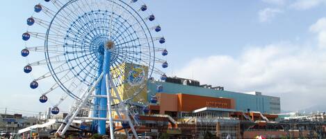 A large Ferris wheel with a blue and white color scheme, surrounded by a waterfront promenade with a bridge and buildings in the background.