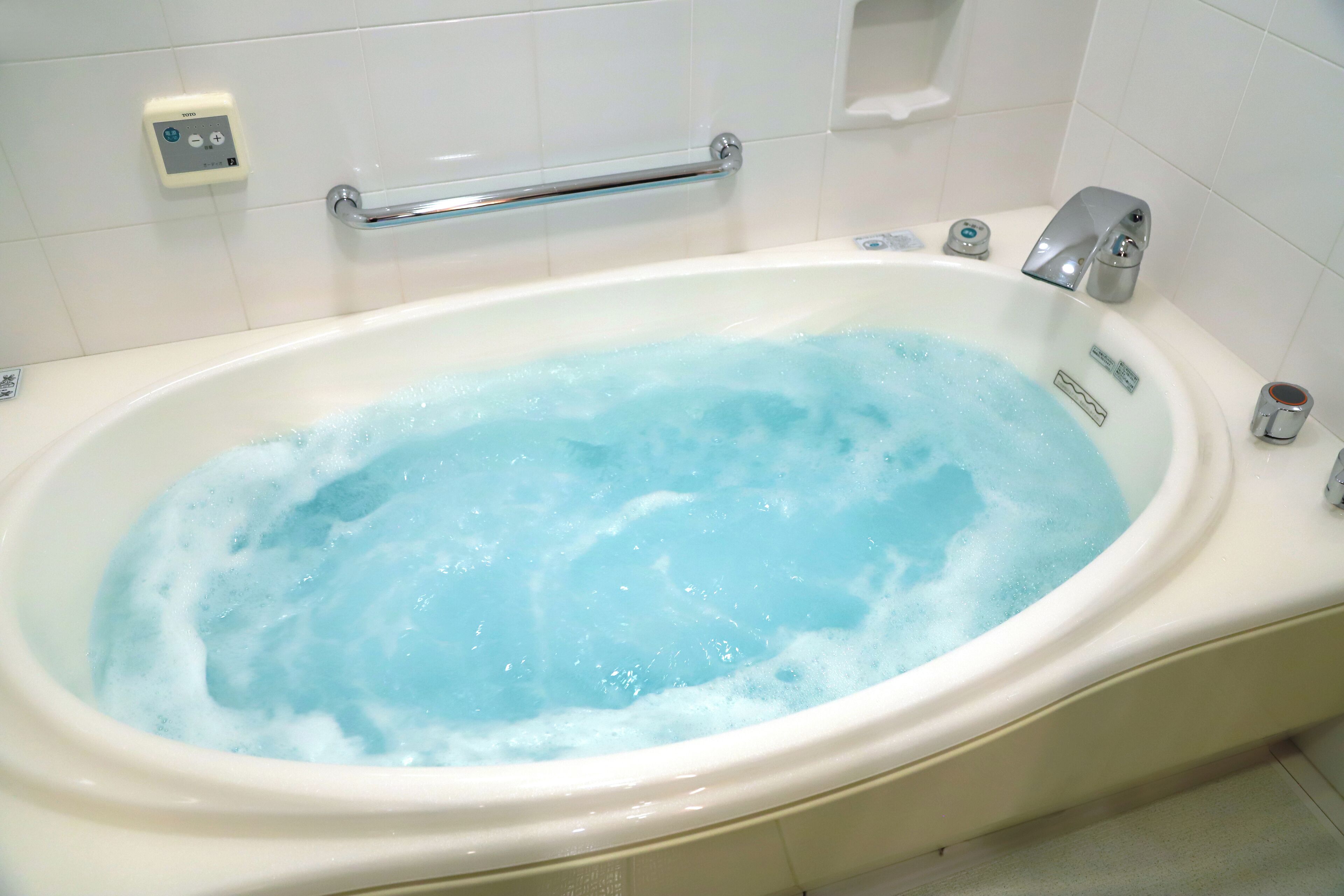 A bathtub with running water, a control panel, and a handrail.