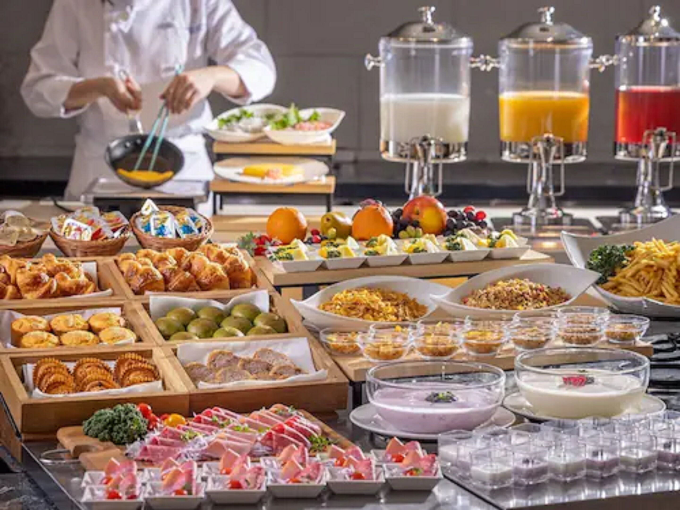 A buffet with various food items, including fruits, pastries, and meats, and beverages in dispensers.