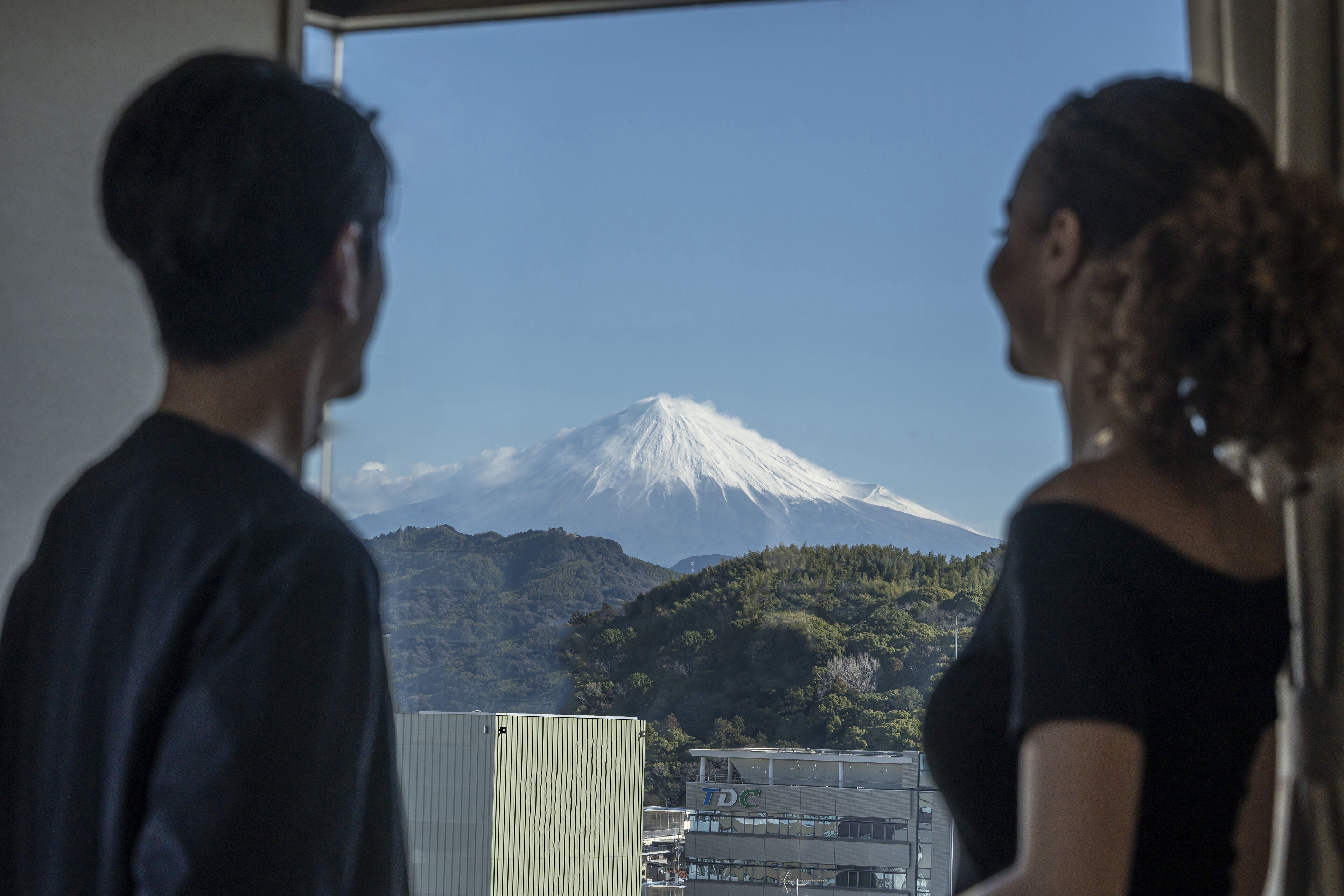 Two people looking out a window at a snow-capped mountain.