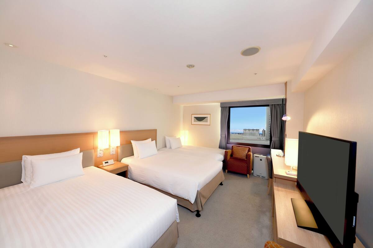 Une chambre d’hôtel avec deux lits, un bureau avec un ordinateur, une télévision et une fenêtre donnant sur un beau paysage.