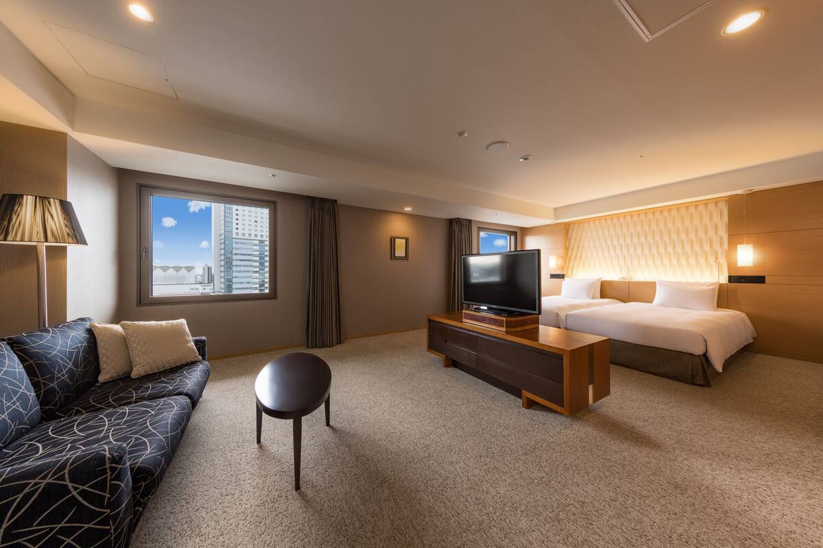 Une chambre d’hôtel équipée d’un canapé, d’un lit, d’une télévision, d’une table basse et d’une fenêtre donnant sur la ville.