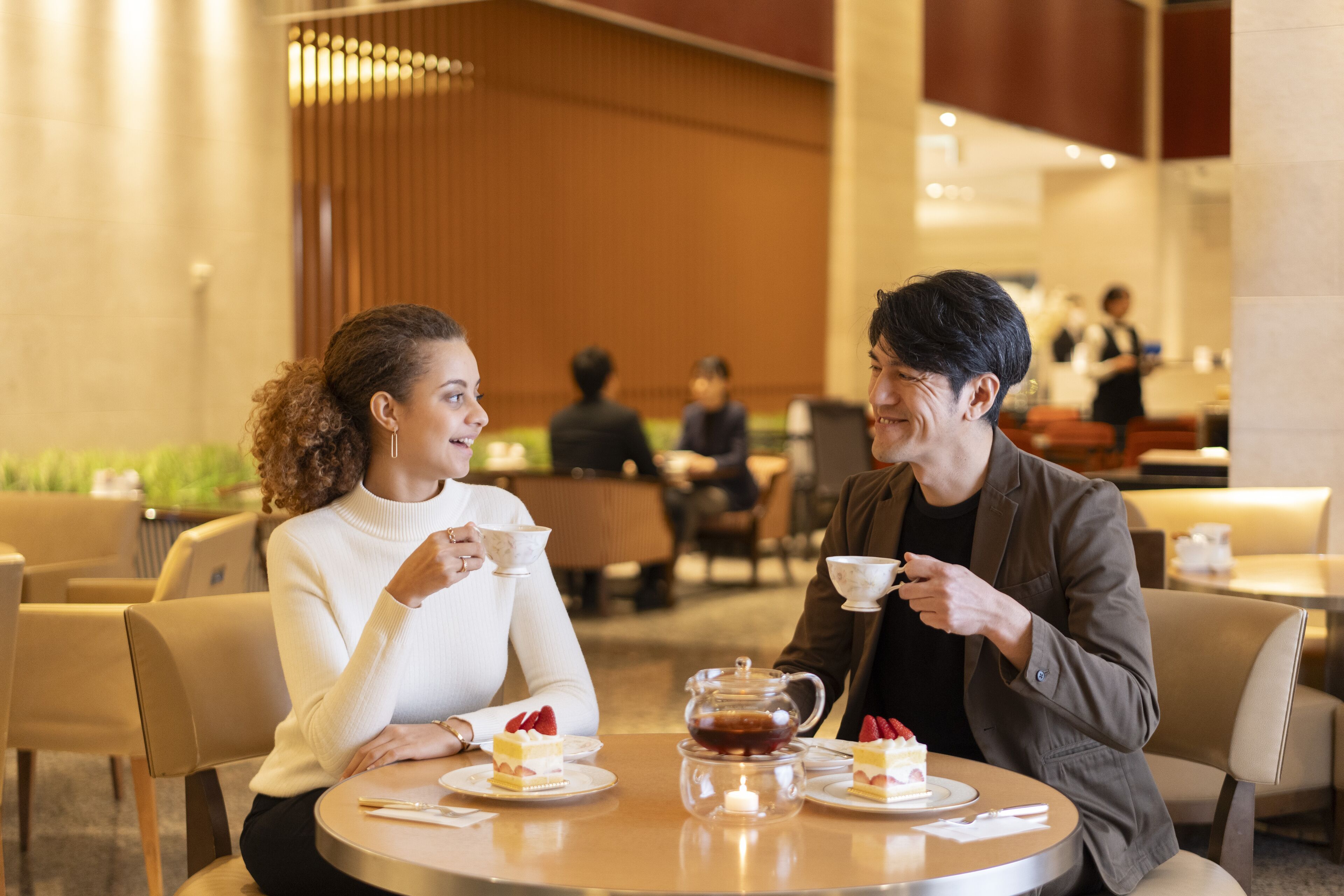 A couple dining at a round table in a modern indoor setting with wooden accents and other diners in the background.