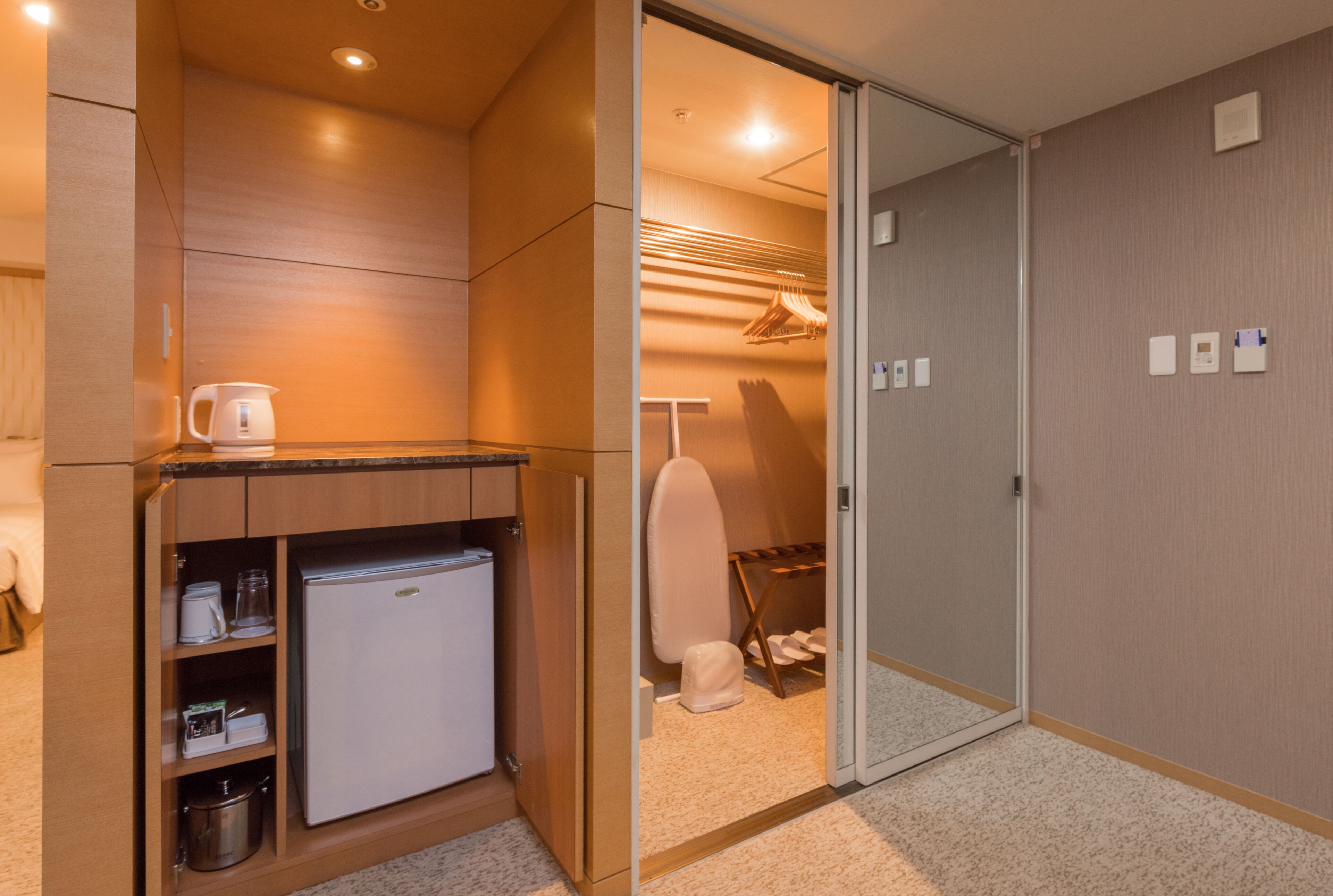 A compact hotel room with a kitchenette, a wardrobe, and a shower area.