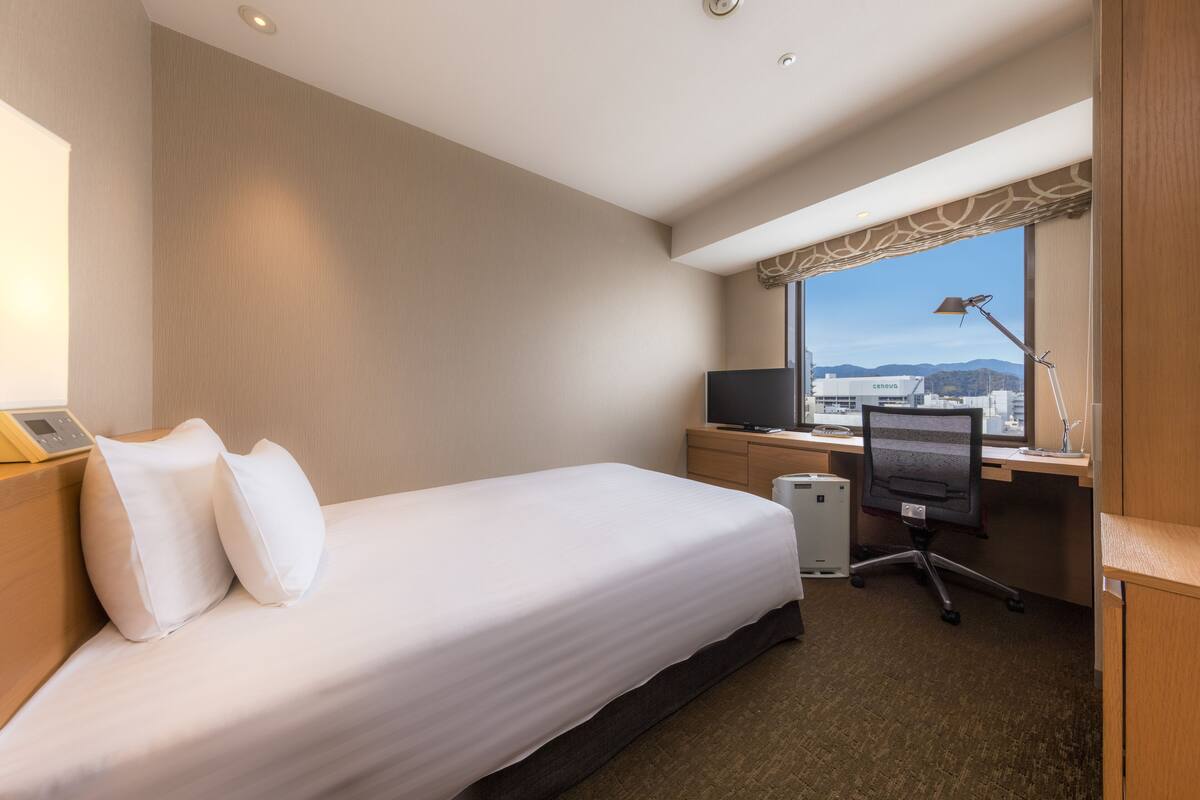 Une chambre d’hôtel équipée d’un lit, d’un bureau, d’une chaise, d’une télévision et offrant une vue sur la ville.