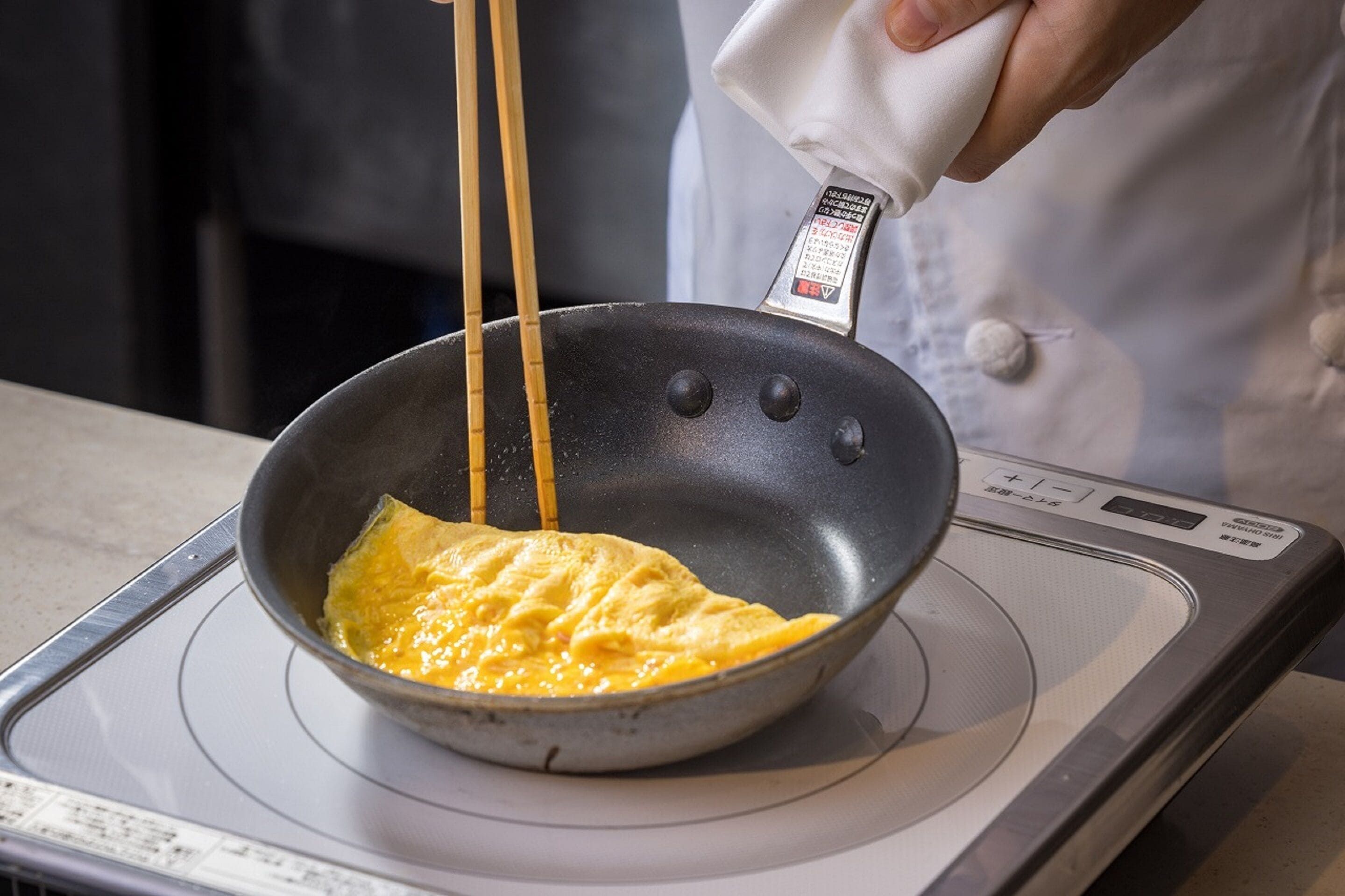 A person cooking an omelette in a non-stick pan on a kitchen stove.