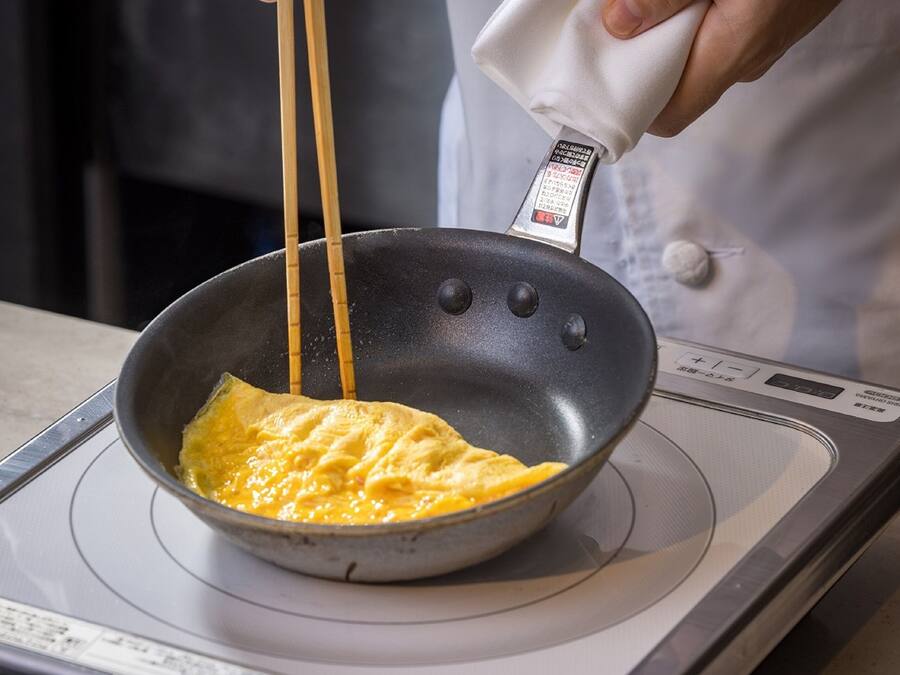 A person cooking an omelette in a non-stick pan on a kitchen stove.