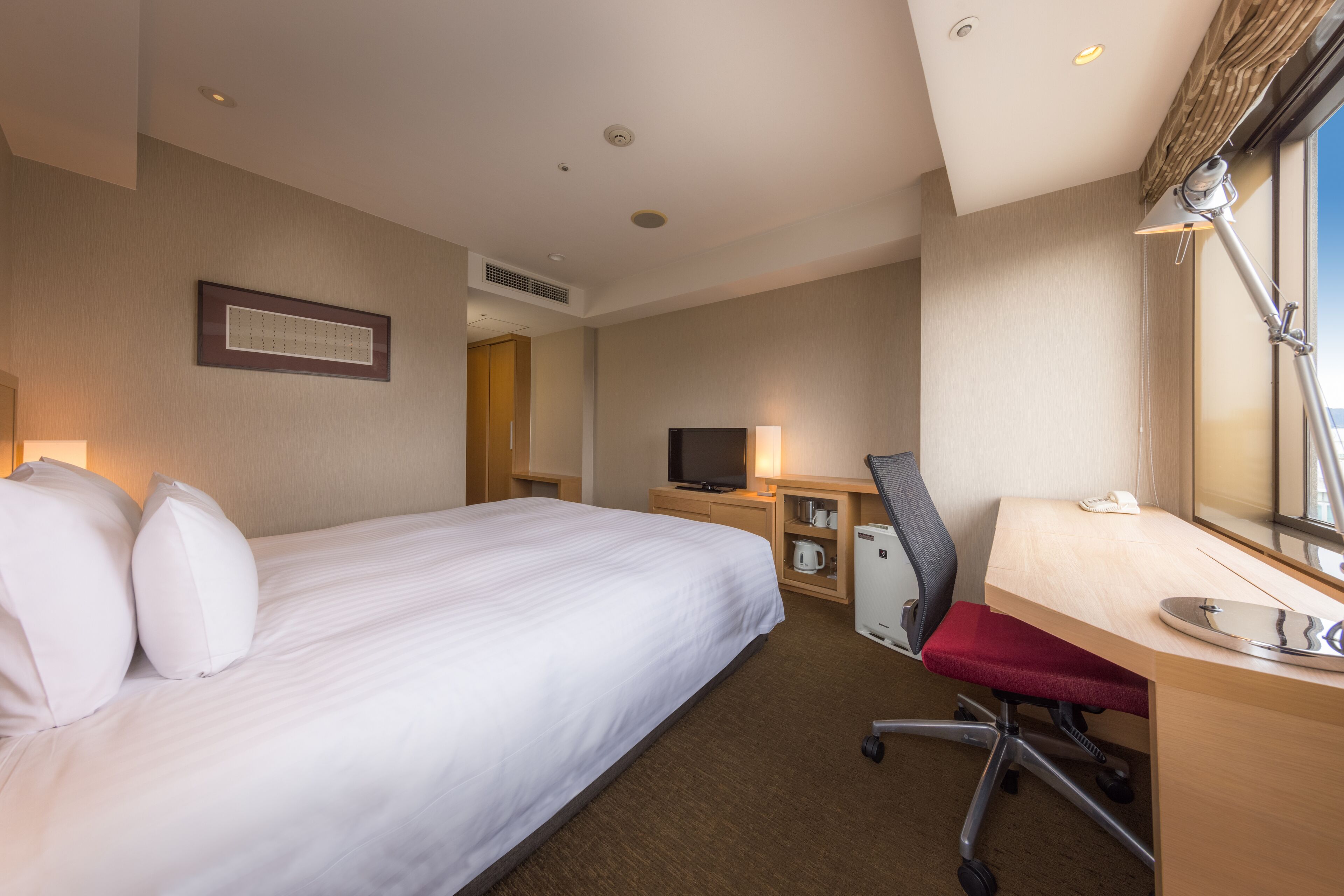 Een hotelkamer met een groot bed, een bureau met stoel, een televisie en een raam.