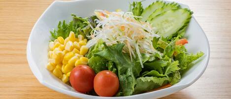 A white bowl containing a salad with lettuce, cucumber, shredded carrots, corn, and tomatoes.