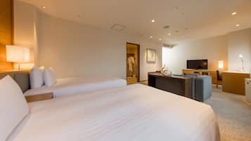 A hotel room with a large bed, a desk with a chair, a television, and a bathroom visible through an open door.