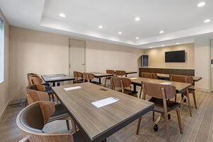 Un salón de conferencias con varias mesas y sillas, una puerta, un televisor de pantalla plana montado en la pared e iluminación empotrada en el techo.