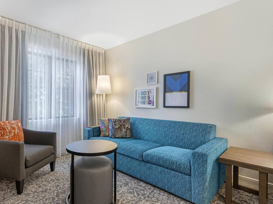 Een hotelkamer met een grijze fauteuil, een blauwe bank, een klein rond tafeltje en een lamp. Er hangen twee ingelijste foto's aan de muur.
