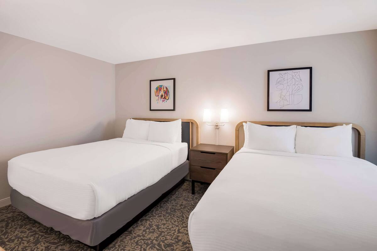 A hotel room with two beds, a nightstand, and two wall-mounted lamps.