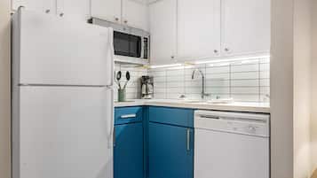 Una cocina con armarios blancos, una encimera azul, microondas, cafetera y lavavajillas.