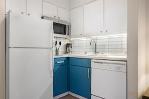 Una cocina con armarios blancos, una encimera azul, microondas, cafetera y lavavajillas.