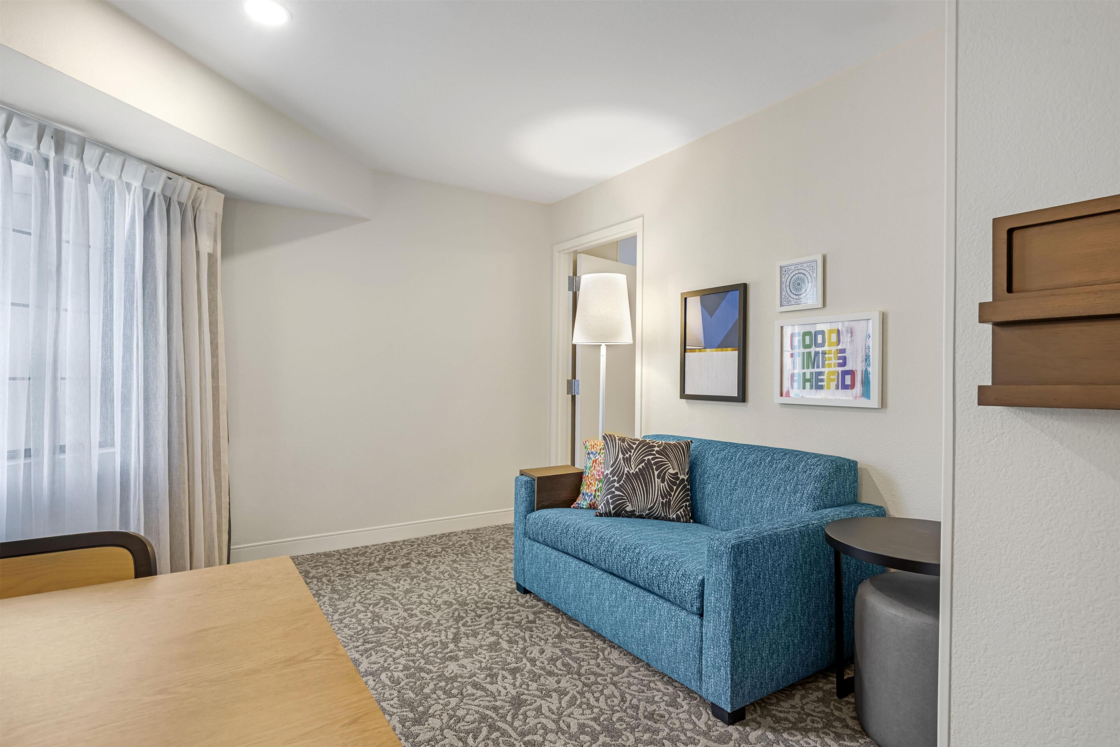 A room with a blue sofa, a wooden table, a patterned rug, and a lamp.